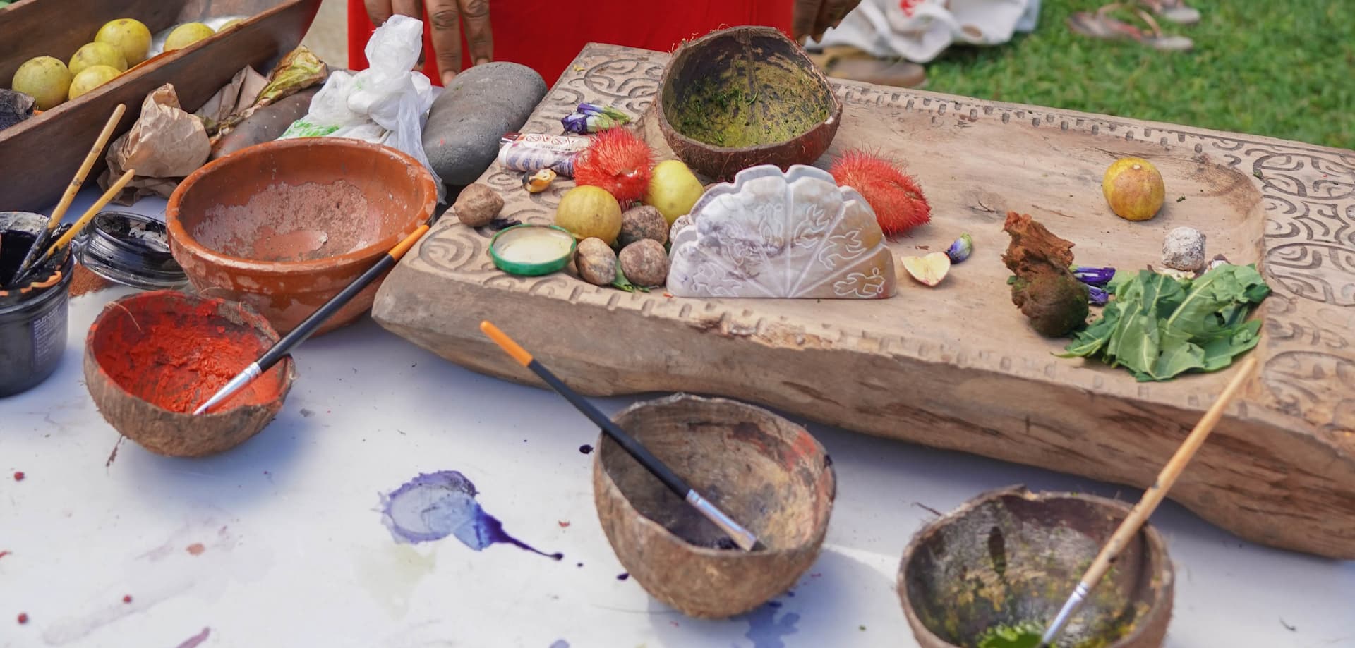 Atelier de fabrication de peintures naturelles à Tahiti. 4 noix de coco avec peintures naturelles et pinceaux posés sur une table. Immersion dans l'Art Polynésien : Tatouages, Sculptures, et Peintures.