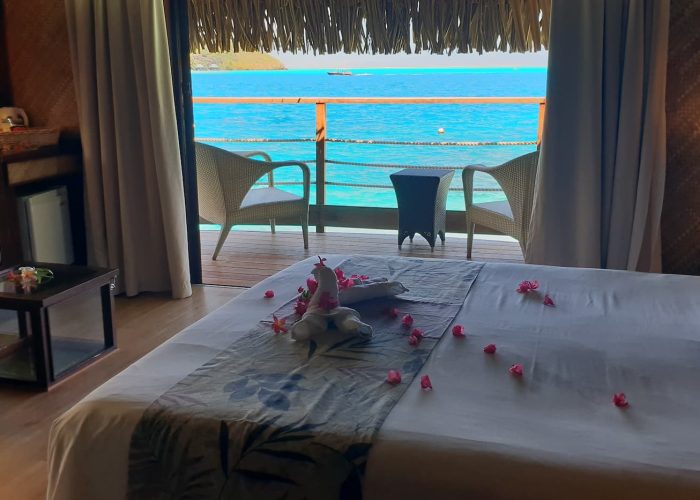 Vue depuis l'intérieur d'un bungalow sur pilotis, lit double fleuri, lagon turquoise - Hôtel Maitai Polynesia Bora Bora 3***